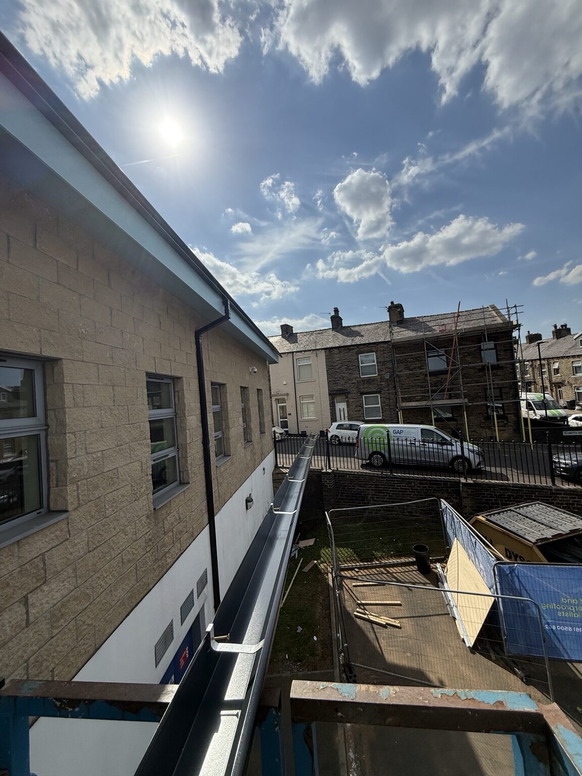 Continuous dark aluminium gutter being installed along a commercial roofline from an access lift