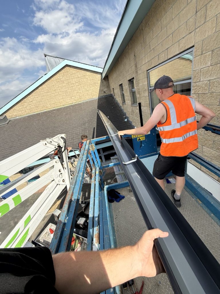 Roofing and guttering team installing a continuous aluminium gutter run from a platform